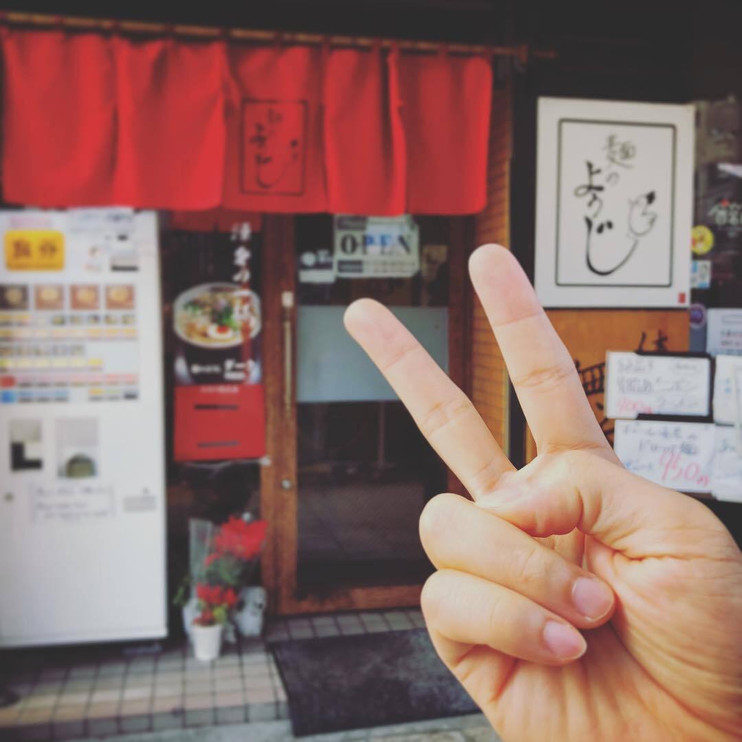 赤いのれんの店先と、ピースサイン