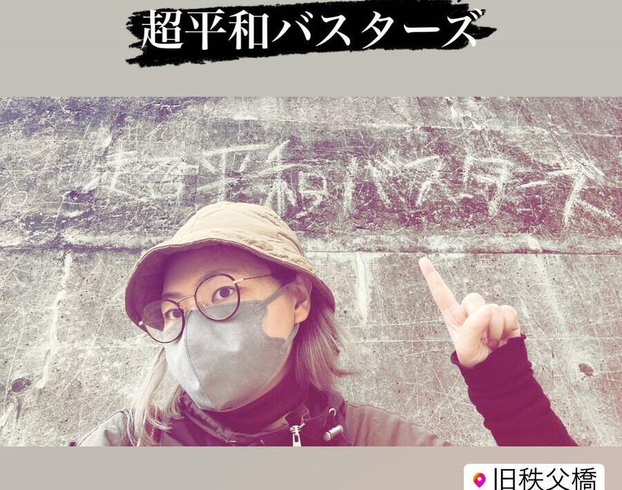 コンクリートに書かれた「超平和バスターズ」と、指さすカエル