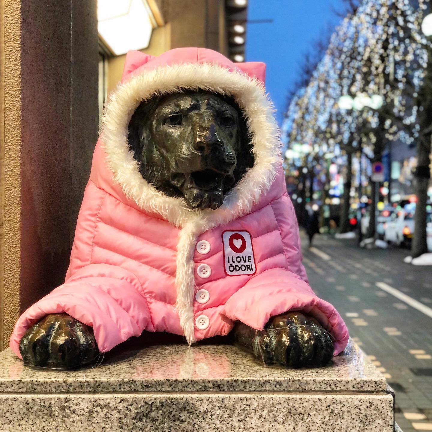 ピンクのダウンを着せてもらった、犬の像