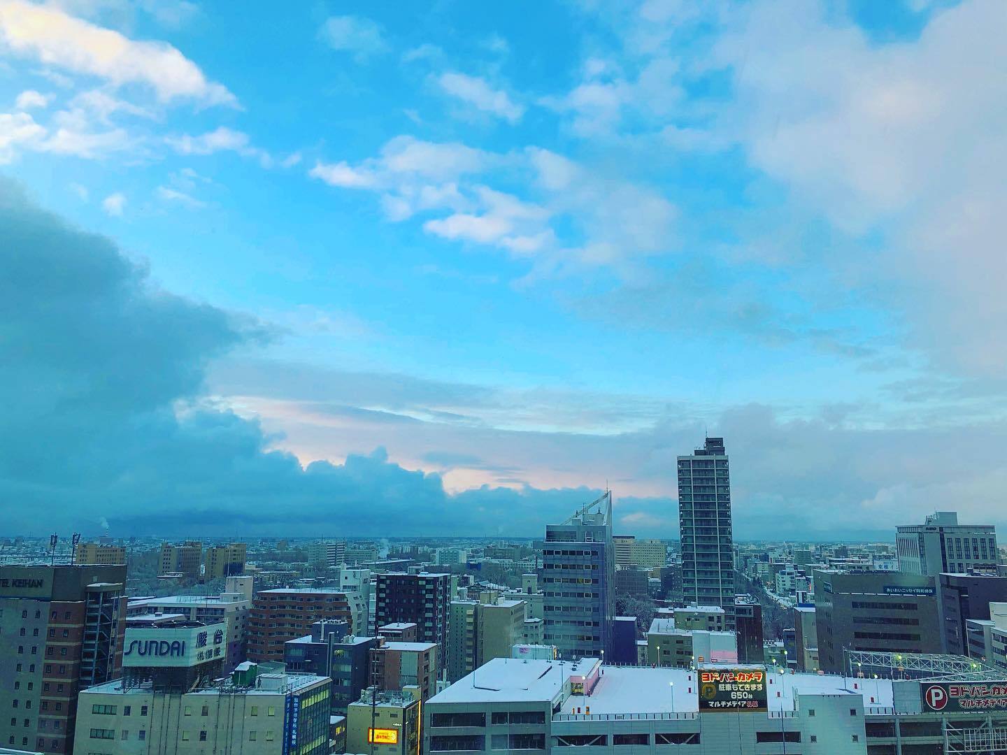 窓から見た、雲の多い空と札幌のビル